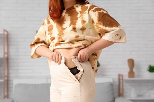 Image of woman trying to do her trousers up after pregnancy weight gain Boston