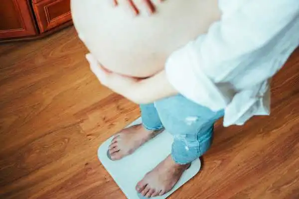 Image of woman weighing herself and experiencing weight gain through pregnancy Boston